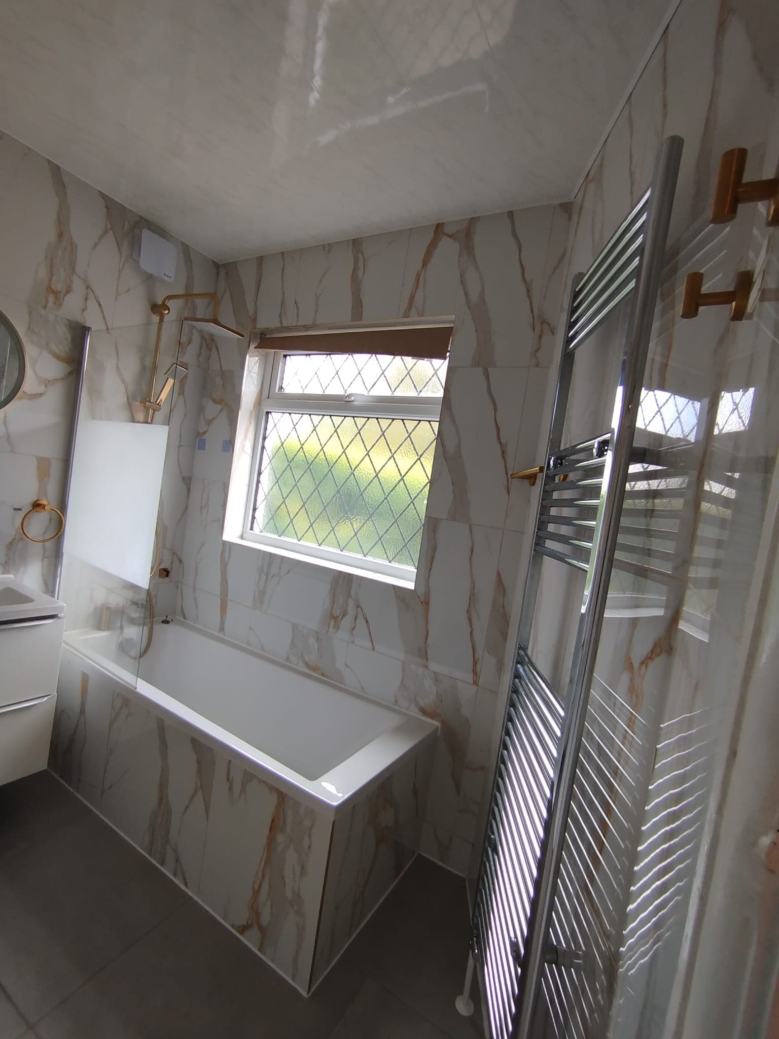 Bath under the window with marble surround and chrome heated towel rail