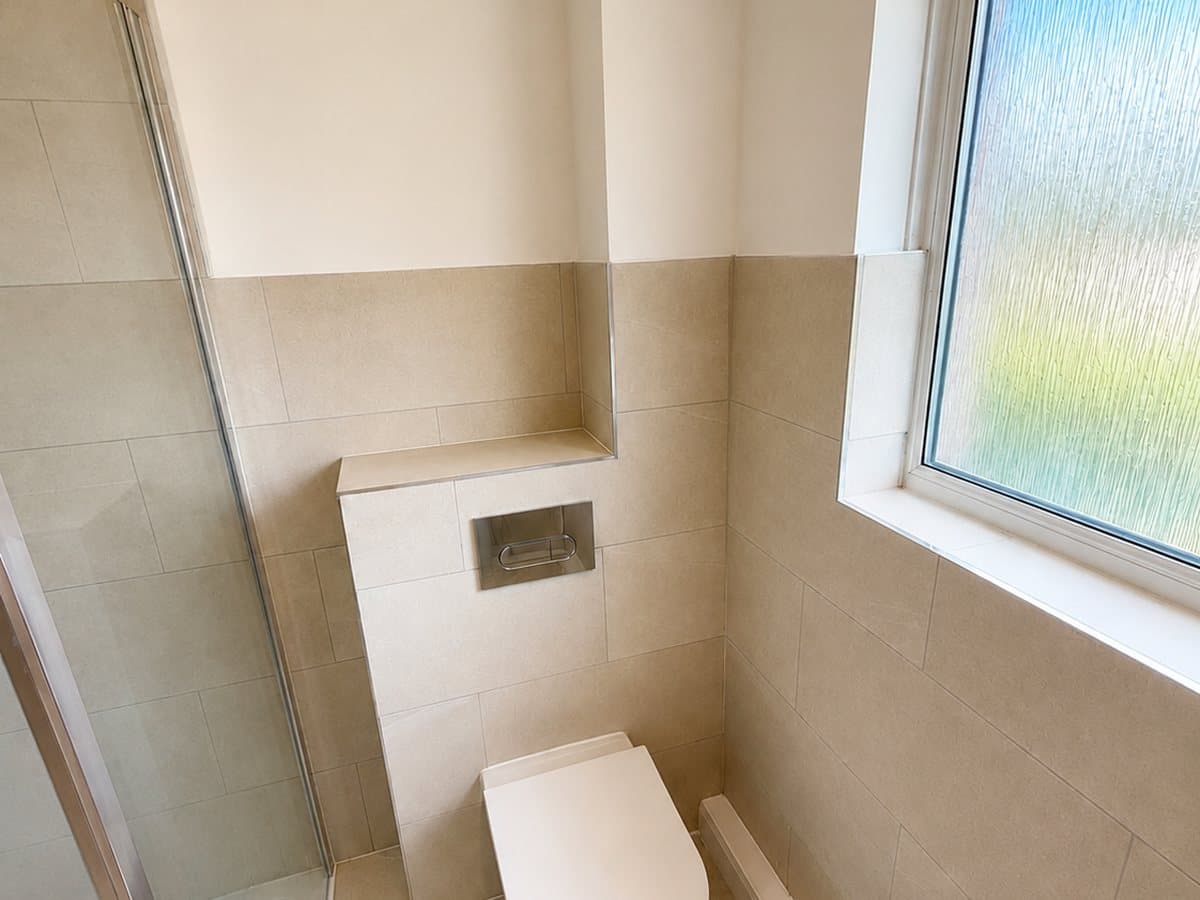 Concealed-cistern WC beside the walk-in shower under a frosted window