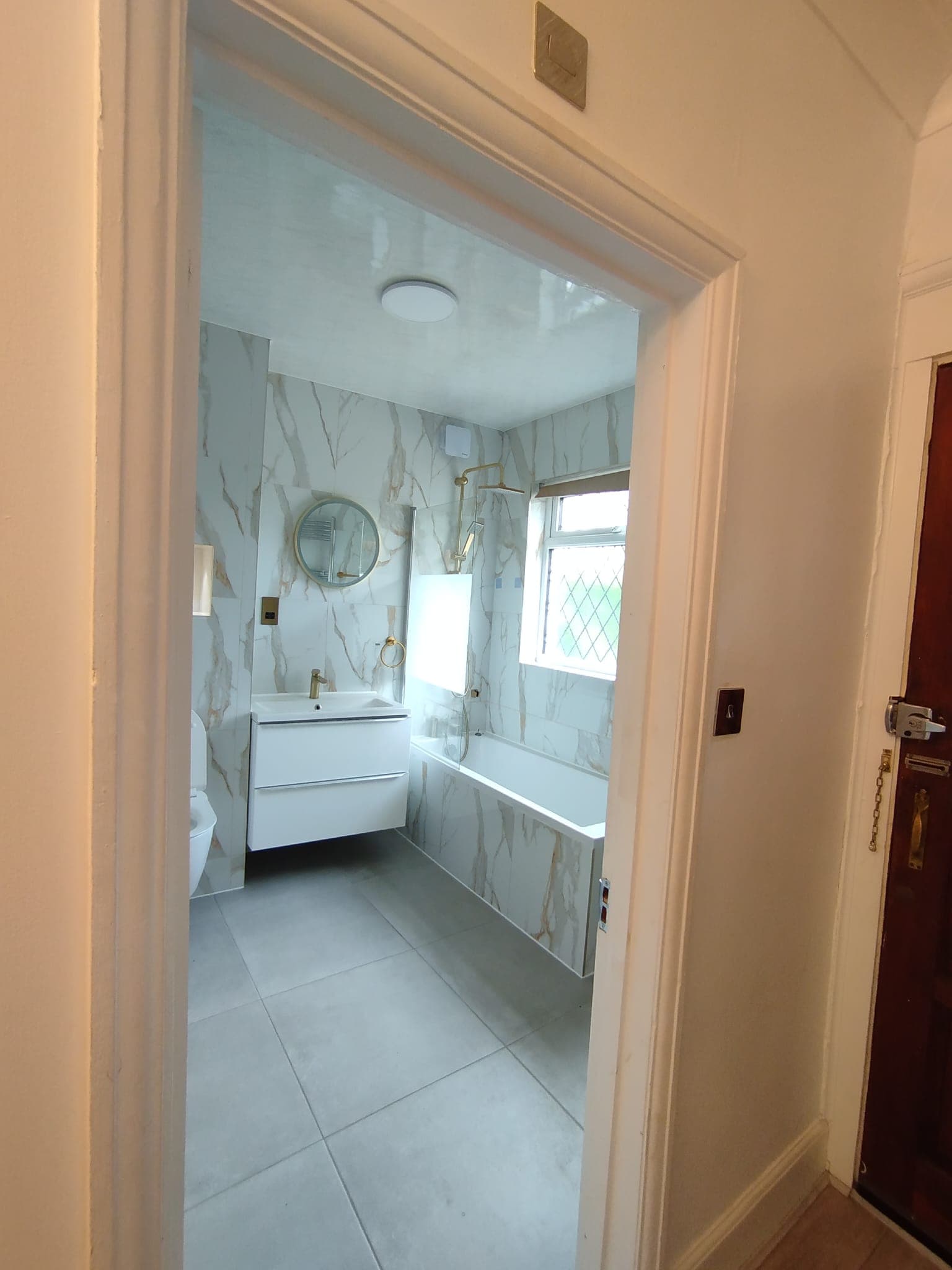 Renovated bathroom with calacatta marble walls, bath, brushed brass fittings and round mirror